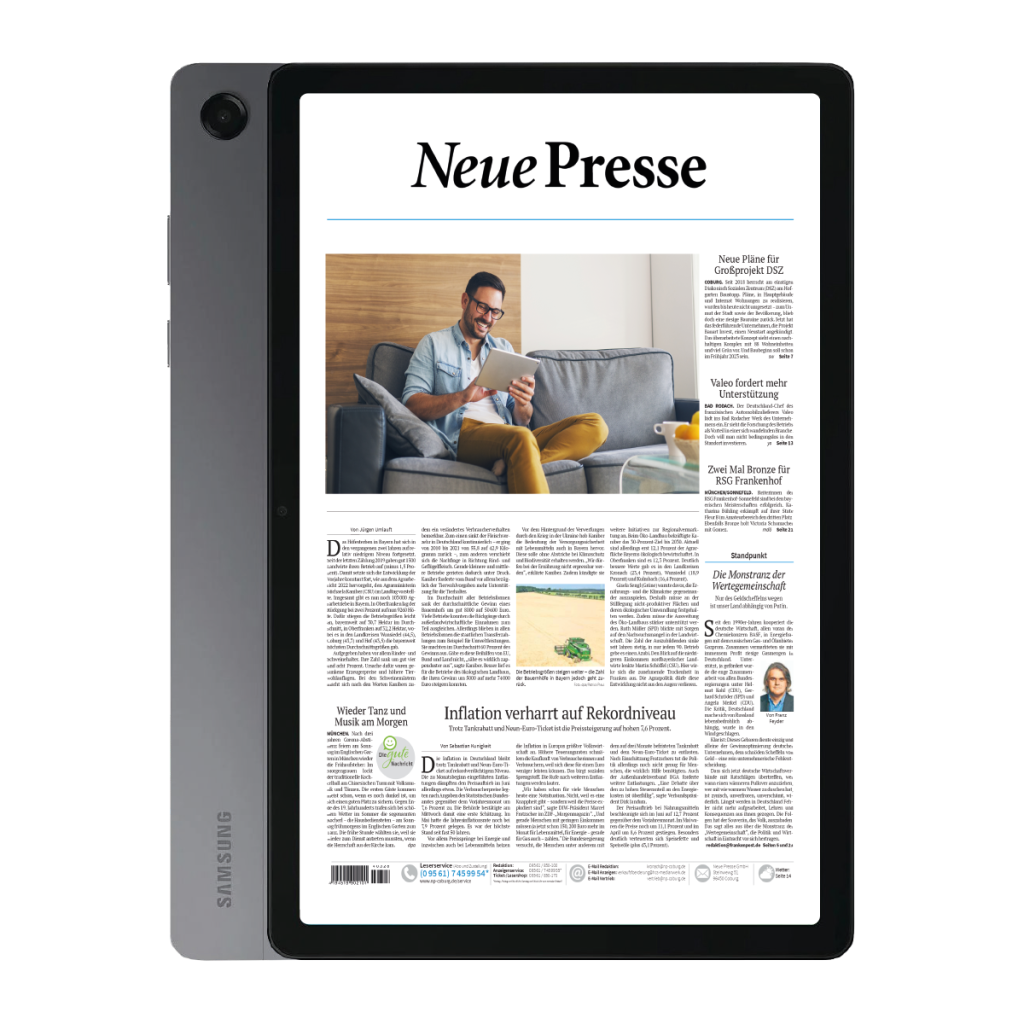 Tablet showing a newspaper layout titled 'Neue Presse' on a screen, with a man reading on a gray sofa in a living room.